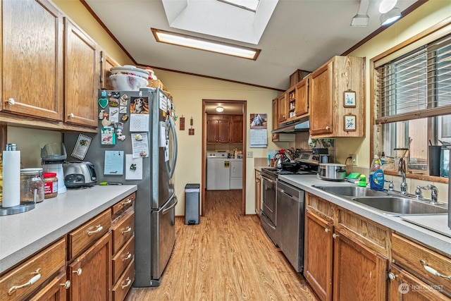 kitchen with appliances with stainless steel finishes, light wood-type flooring, lofted ceiling with skylight, washer and clothes dryer, and sink