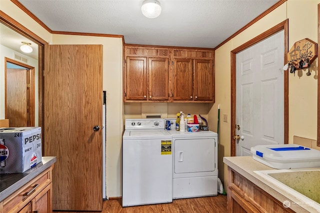 laundry room with cabinets, light hardwood / wood-style flooring, washer and dryer, ornamental molding, and a textured ceiling