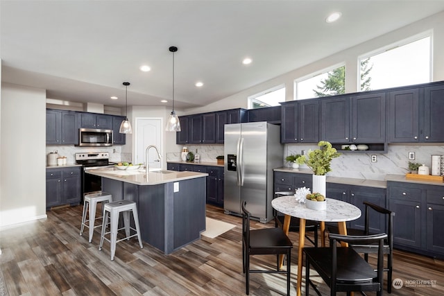 kitchen with backsplash, a center island with sink, vaulted ceiling, and appliances with stainless steel finishes