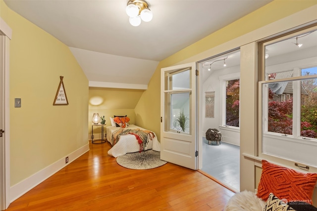 bedroom featuring lofted ceiling, light hardwood / wood-style floors, and rail lighting