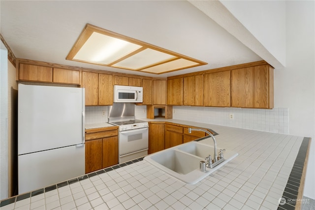 kitchen featuring tasteful backsplash, brown cabinetry, a sink, white appliances, and a peninsula