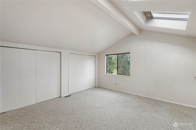 unfurnished bedroom with vaulted ceiling with skylight, carpet, and multiple closets