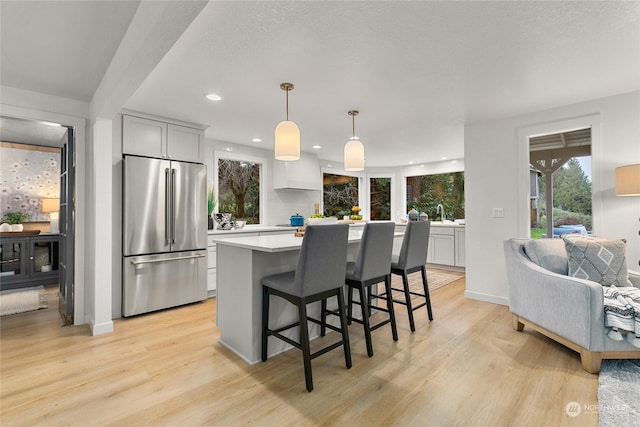 kitchen with a kitchen breakfast bar, stainless steel fridge, light hardwood / wood-style floors, and hanging light fixtures