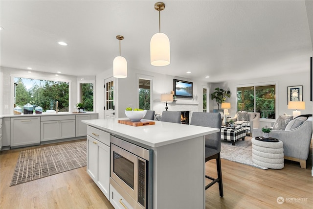 kitchen featuring pendant lighting, stainless steel microwave, light wood-type flooring, a kitchen island, and a kitchen bar