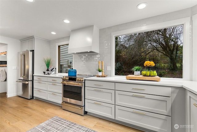 kitchen with custom range hood, backsplash, stainless steel appliances, and light hardwood / wood-style flooring