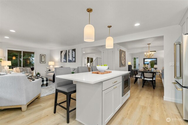 kitchen featuring white cabinets, decorative light fixtures, light wood-type flooring, and stainless steel appliances