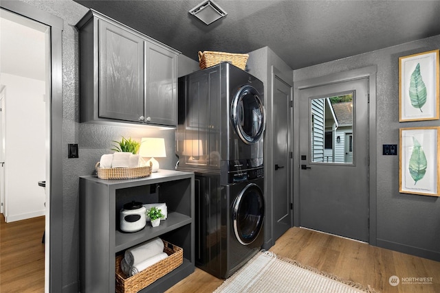 laundry area with cabinets, a textured ceiling, light wood-type flooring, and stacked washing maching and dryer