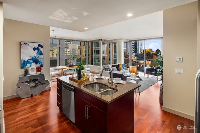 kitchen with dark wood-type flooring, a center island with sink, sink, stainless steel dishwasher, and light stone countertops