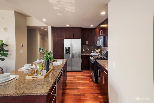 kitchen featuring hardwood / wood-style floors, decorative backsplash, sink, light stone countertops, and appliances with stainless steel finishes