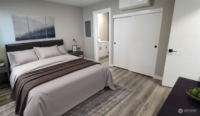 bedroom with an AC wall unit, connected bathroom, hardwood / wood-style floors, and electric panel