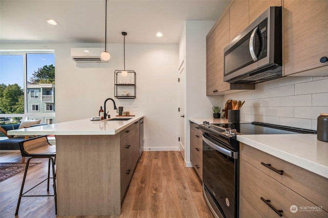 kitchen with a wall unit AC, light hardwood / wood-style flooring, sink, pendant lighting, and appliances with stainless steel finishes