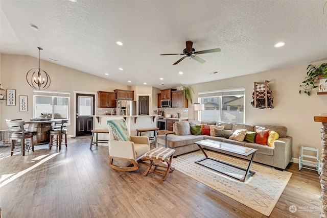 living room featuring ceiling fan with notable chandelier, light wood-type flooring, lofted ceiling, and a textured ceiling