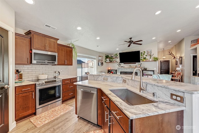 kitchen with ceiling fan, sink, stainless steel appliances, an island with sink, and light wood-type flooring