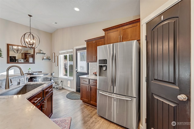 kitchen featuring sink, hanging light fixtures, stainless steel refrigerator with ice dispenser, light hardwood / wood-style floors, and lofted ceiling