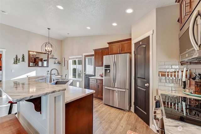 kitchen featuring sink, light wood-type flooring, appliances with stainless steel finishes, decorative light fixtures, and a kitchen bar