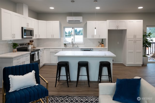 kitchen featuring white cabinets, an AC wall unit, pendant lighting, a kitchen island, and appliances with stainless steel finishes