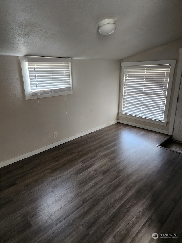 unfurnished room with lofted ceiling, dark wood-type flooring, and a textured ceiling