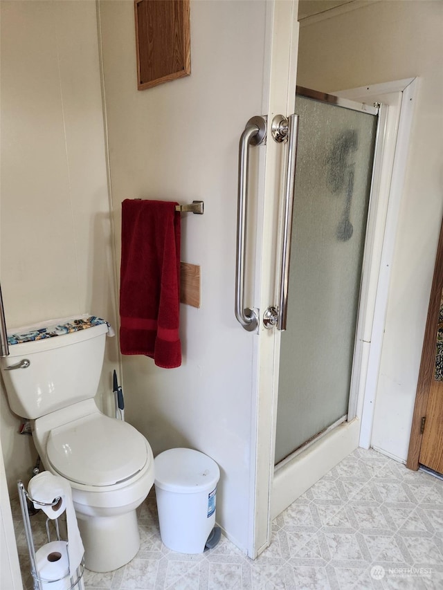 bathroom featuring toilet and a shower with door