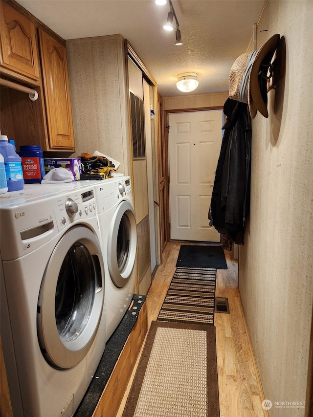 washroom featuring a textured ceiling, cabinets, rail lighting, washer and dryer, and light hardwood / wood-style flooring