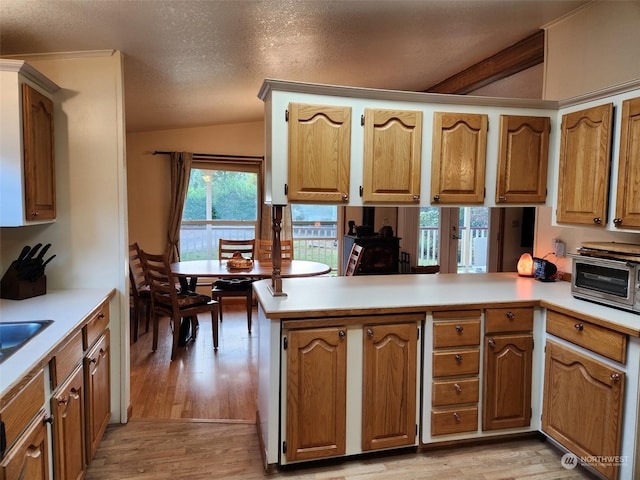 kitchen with light wood-type flooring, kitchen peninsula, vaulted ceiling, and a textured ceiling