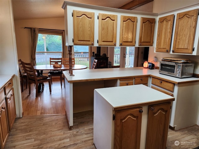 kitchen featuring kitchen peninsula, vaulted ceiling, light hardwood / wood-style floors, and a center island