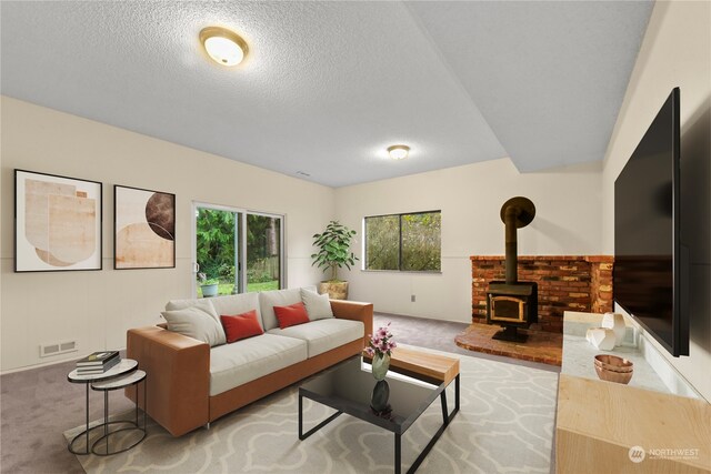 living room with a wood stove, light colored carpet, a healthy amount of sunlight, and a textured ceiling