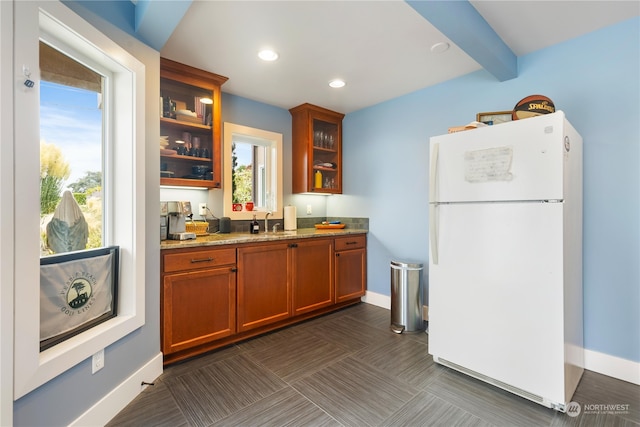 kitchen with glass insert cabinets, light stone counters, freestanding refrigerator, beam ceiling, and a sink