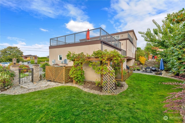 back of house featuring a lawn, a patio, a balcony, and stucco siding