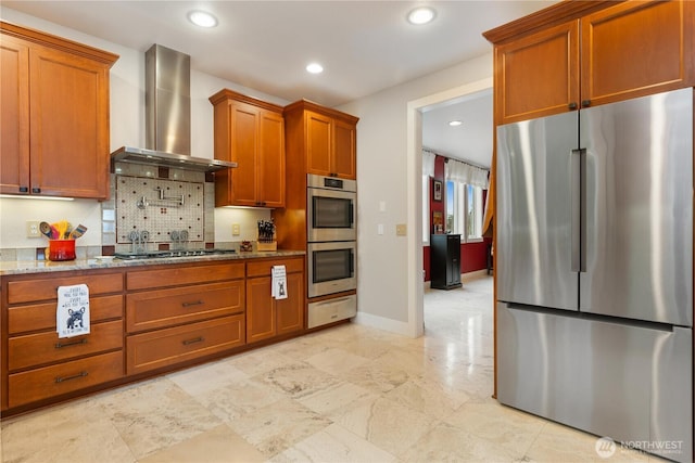 kitchen with light stone counters, brown cabinets, stainless steel appliances, recessed lighting, and wall chimney range hood