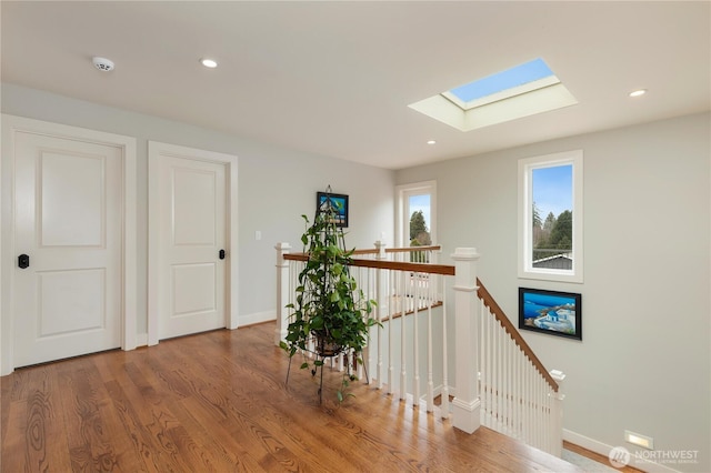 hall with recessed lighting, a skylight, wood finished floors, an upstairs landing, and baseboards