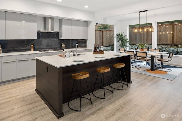 kitchen featuring tasteful backsplash, decorative light fixtures, wall chimney range hood, and light wood-type flooring