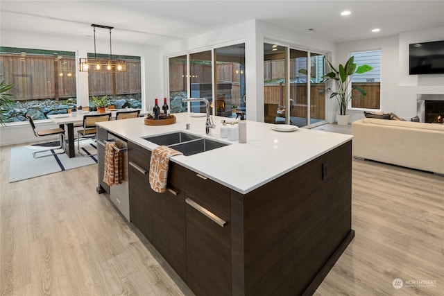 kitchen featuring decorative light fixtures, dark brown cabinetry, a kitchen island with sink, and light hardwood / wood-style flooring