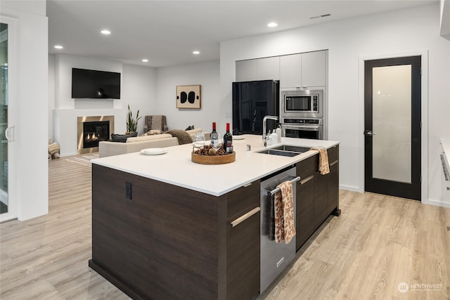 kitchen featuring sink, light hardwood / wood-style flooring, a center island with sink, dark brown cabinets, and appliances with stainless steel finishes