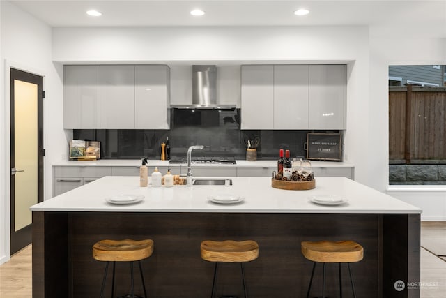 kitchen with a kitchen bar, a kitchen island with sink, and wall chimney exhaust hood