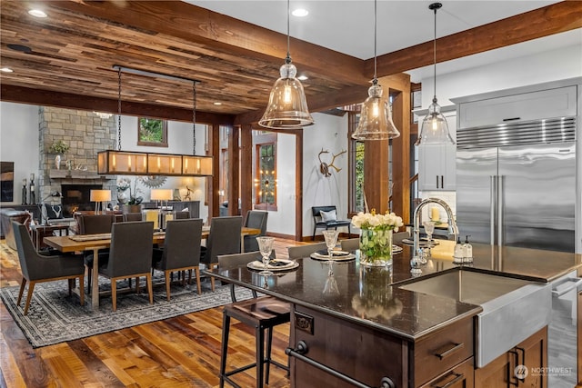 kitchen with stainless steel appliances, a stone fireplace, dark hardwood / wood-style floors, dark stone counters, and a kitchen island