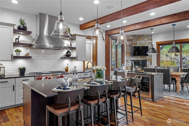 kitchen featuring pendant lighting, a center island with sink, wall chimney range hood, light wood-type flooring, and a fireplace