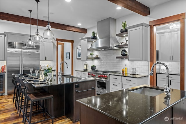 kitchen with beamed ceiling, high quality appliances, ventilation hood, and an island with sink