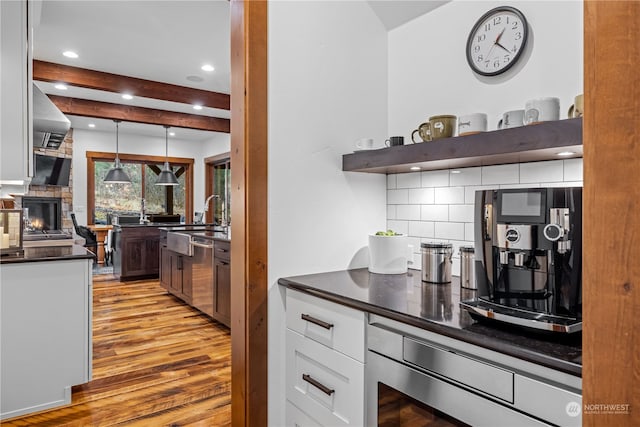 kitchen featuring beam ceiling, hanging light fixtures, tasteful backsplash, light hardwood / wood-style floors, and white cabinets