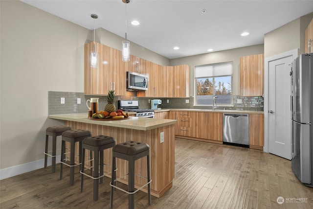 kitchen with hanging light fixtures, light hardwood / wood-style flooring, kitchen peninsula, a breakfast bar area, and stainless steel appliances