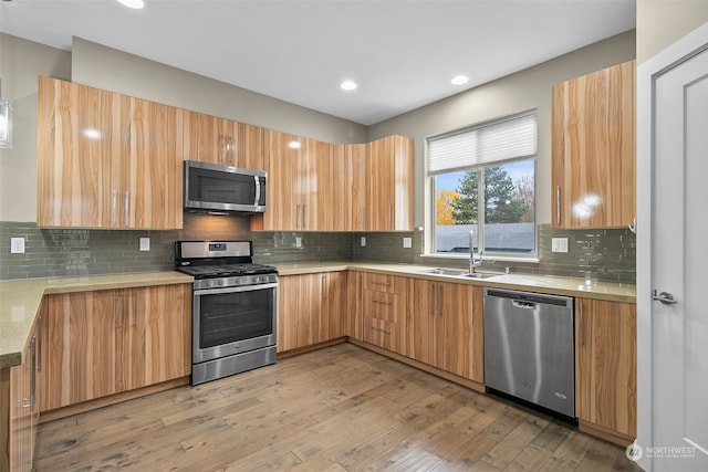 kitchen with decorative backsplash, appliances with stainless steel finishes, light wood-type flooring, and sink