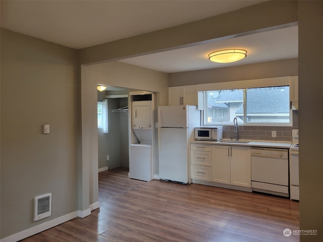 kitchen featuring white cabinets, white appliances, stacked washer / drying machine, and sink