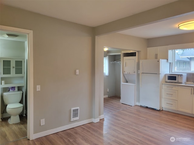 kitchen with a healthy amount of sunlight, white appliances, white cabinetry, and stacked washer / drying machine