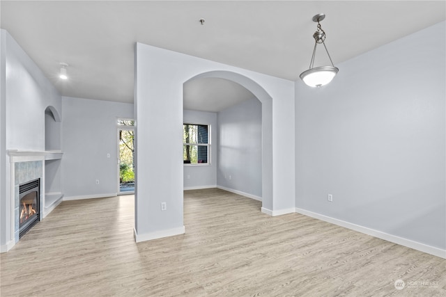 unfurnished living room with a tiled fireplace and light hardwood / wood-style flooring