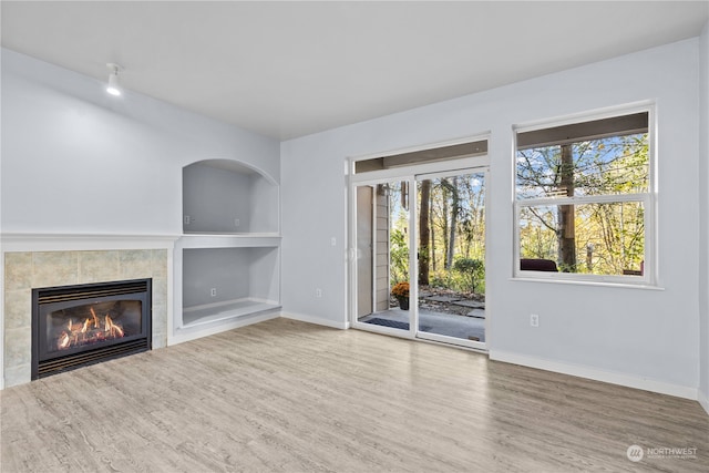 unfurnished living room featuring built in shelves, wood-type flooring, and a fireplace