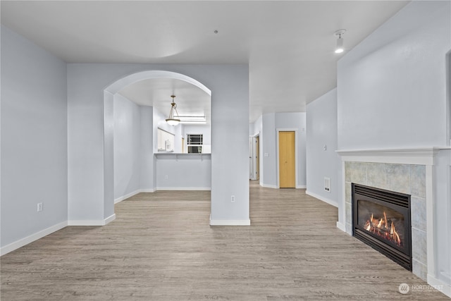 unfurnished living room with light wood-type flooring and a tiled fireplace