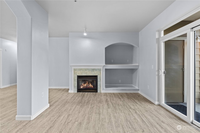 unfurnished living room featuring a tiled fireplace, built in features, and light hardwood / wood-style flooring