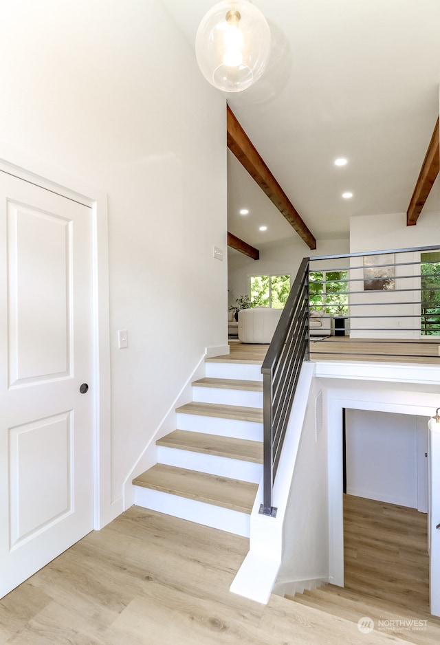 stairs featuring beamed ceiling and hardwood / wood-style floors