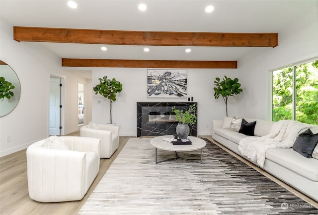 living room with a tile fireplace, beamed ceiling, and light wood-type flooring