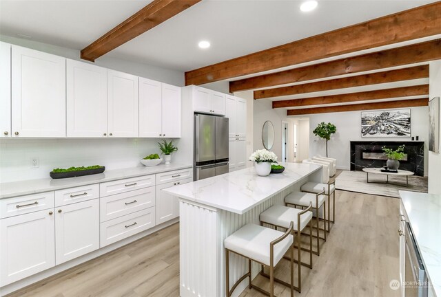 kitchen featuring a kitchen breakfast bar, stainless steel fridge, white cabinetry, and beam ceiling