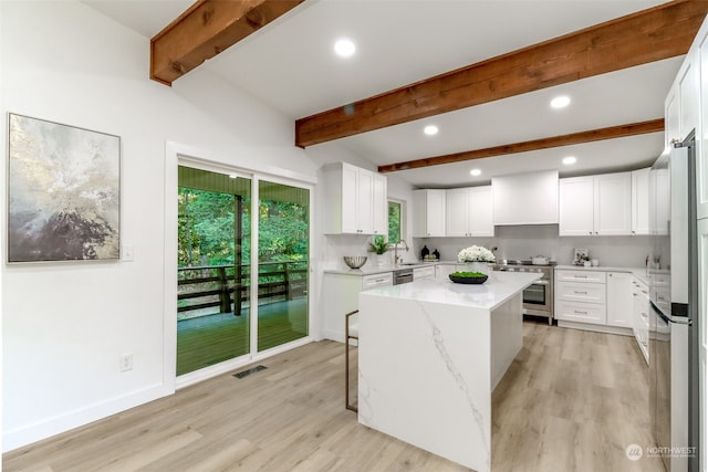 kitchen featuring appliances with stainless steel finishes, light stone counters, light hardwood / wood-style flooring, white cabinets, and a center island